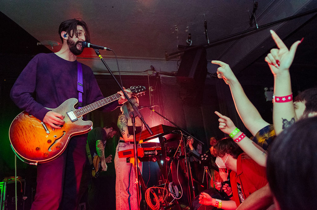 tigers jaw playing at market hotel in Brooklyn with singer Ben Walsh on the left wearing a purple sweater playing guitar and the audience on the right with their arms up