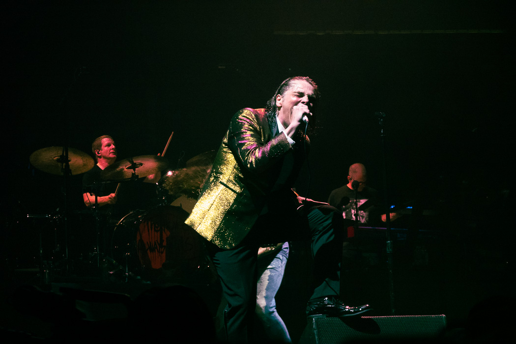 Gerard Way singing at NJ concert wearing a glittery yellow and red blazer. Behind him is drummer Jarrod Alexander to his left and keyboardist Jamie Muhoberac to his right.